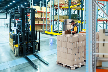 Poster - Man warehouse contractor. Forklift inside storehouse. Warehouse with cardboard boxes on pallets. Storeroom of courier company. Man storekeeper at distribution warehouse. Forklift for storage