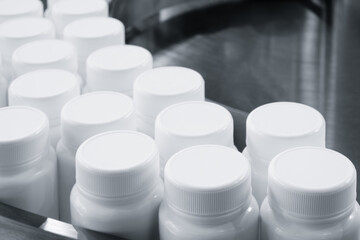 Poster - Row of white plastic containers with lids for medicines or vitamins or active dietary supplements on conveyor belt of pharmaceutical factory
