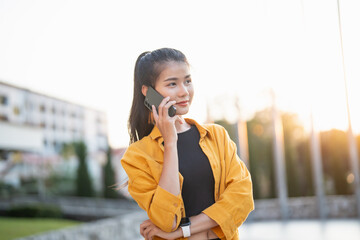 Wall Mural - Smiling young Asian woman using smartphone in urban city checking apps mobile outdoors