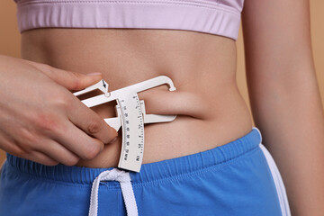 Wall Mural - Woman measuring body fat with caliper on beige background, closeup