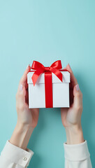 Aufkleber - Female hands hold a small, white giftbox with a red ribbon bow on a soft pastel blue background with plenty of empty space._00002_