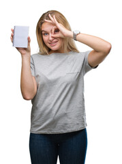 Wall Mural - Young caucasian woman holding blank notebook over isolated background with happy face smiling doing ok sign with hand on eye looking through fingers