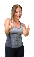 Canvas Print - Beautiful middle age woman wearing sport clothes over isolated background approving doing positive gesture with hand, thumbs up smiling and happy for success. Looking at the camera, winner gesture.