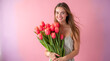 © zamuruev - A young woman with flowing hair joyfully holds a large bouquet of bright tulips, dressed in a soft pastel outfit