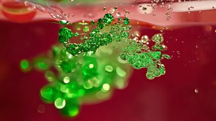 Poster - Dynamic drops of green glitter in red oil or ink diffusing through water, creating an abstract aquatic swirls