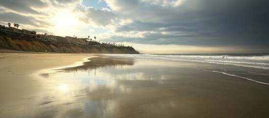 Wall Mural - Serene beach landscape with reflections at sunset highlighting gentle waves and dramatic clouds over the coastline.