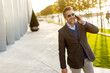 © BGStock72 - Professional man walking confidently outside a modern building while engaging in a phone conversation during a bright afternoon