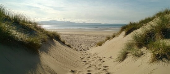 Aufkleber - Tranquil sand dunes leading to a serene beach with gentle waves and distant mountains under a clear sky.