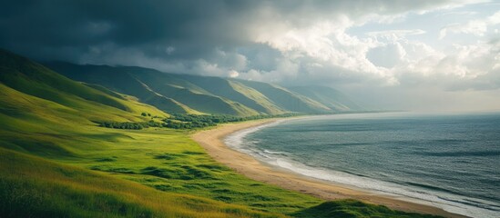 Poster - Scenic coastal view of a sandy beach bordered by lush green hills under a dramatic cloudy sky showcasing nature's beauty.