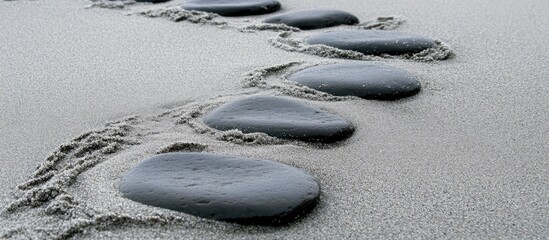 Poster - Footprints in wet sand leading to smooth natural stones on a tranquil beach showcasing coastal beauty and serenity