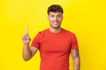 Sticker - Young caucasian handsome man isolated on yellow background showing and lifting a finger in sign of the best