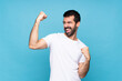 © luismolinero - Young man with beard  over isolated blue background celebrating a victory
