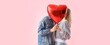 © Pixel-Shot - Happy young couple kissing behind heart-shaped balloon on pink background. Valentine's Day celebration