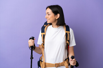 young caucasian woman with backpack and trekking poles isolated on blue background looking side