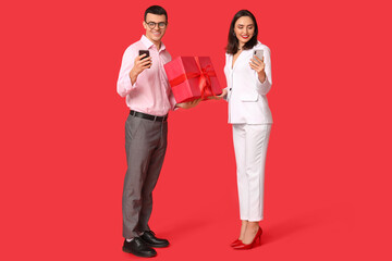 Wall Mural - Young couple with mobile phones and gift box on red background. Online dating