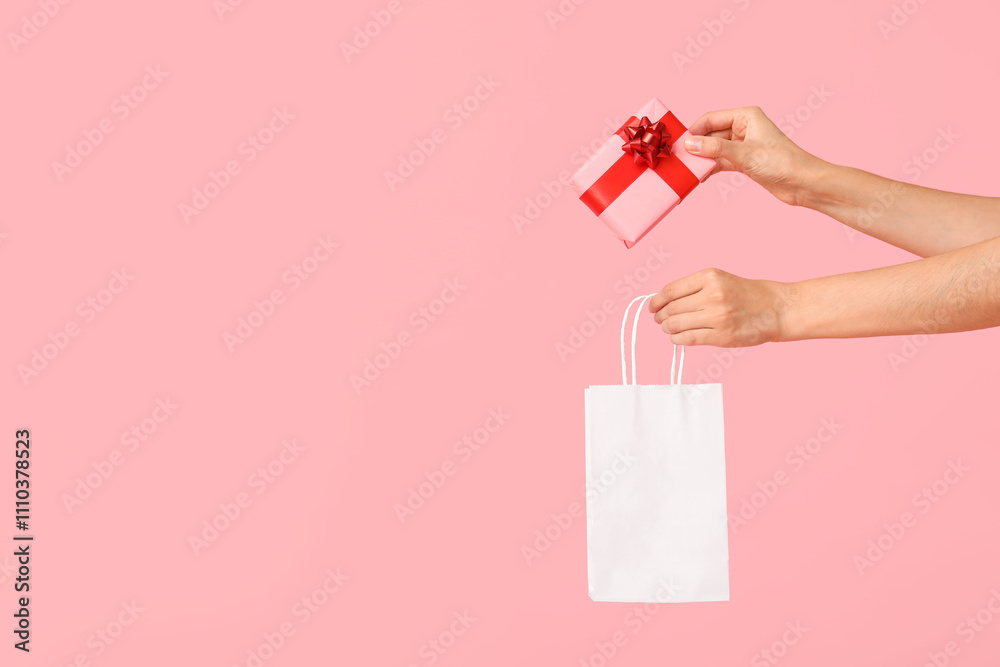 Female hands with gift box and shopping bag on pink background. Valentine's Day celebration