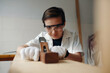 © DragonImages - Boy in protective glasses working with wood tool in workshop