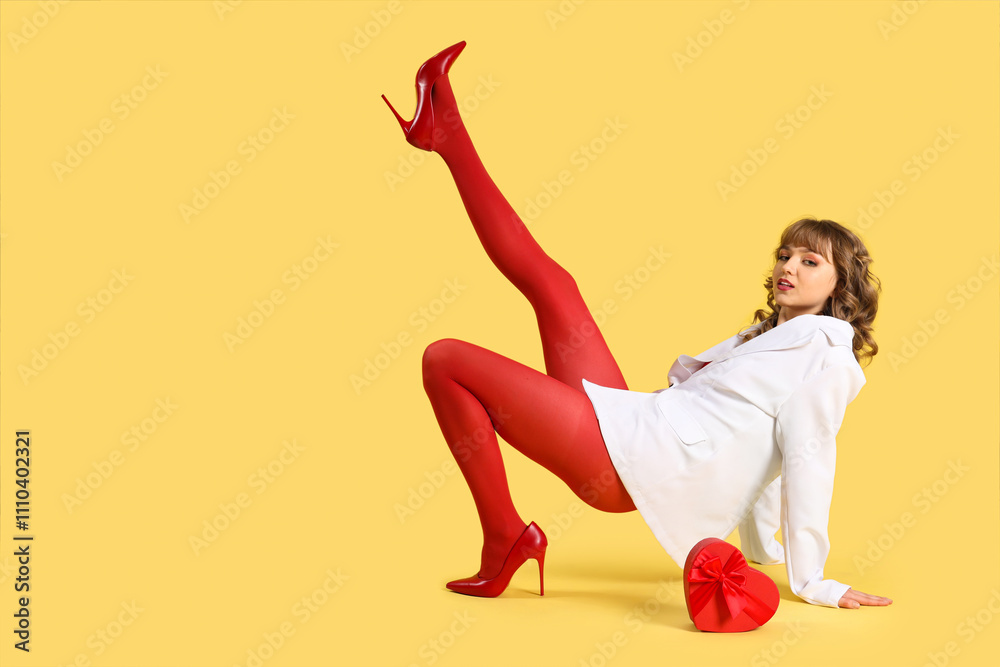 Beautiful young woman with gift box on yellow background. Valentine's Day celebration