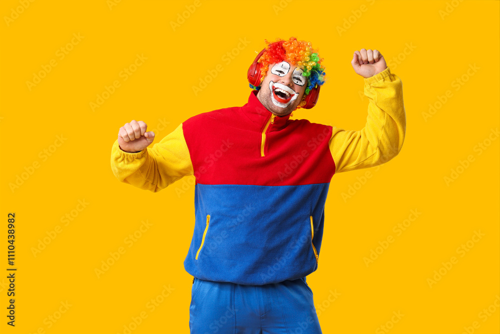 Young man as crazy clown in headphones dancing on yellow background