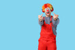 © Pixel-Shot - Young man as bad clown in headphones showing middle fingers on blue background