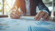 © siyons - Close-up of businessman's hands reviewing financial documents and charts.