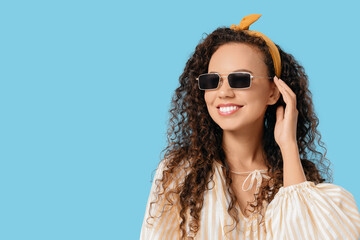 Poster - Beautiful African-American woman with sunglasses on blue background