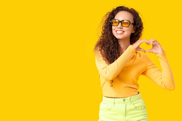 Poster - Beautiful African-American woman with sunglasses making heart with her hands on yellow background