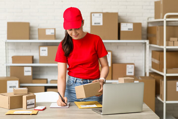 Wall Mural - Female worker with parcel writing in notebook at postal warehouse