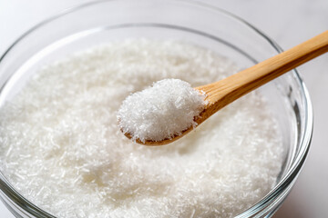 Monosodium glutamate in a wooden spoon over glass bowl full of MSG white crystals close-up. Concept of E621 flavor enhancer food additive.