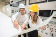 © Nutchapong Wuttisak - Male and female engineers look at blueprints analyzing the structure of wind and water power plants of large industrial plants, wearing hard hats and holding electrical circuit boards.