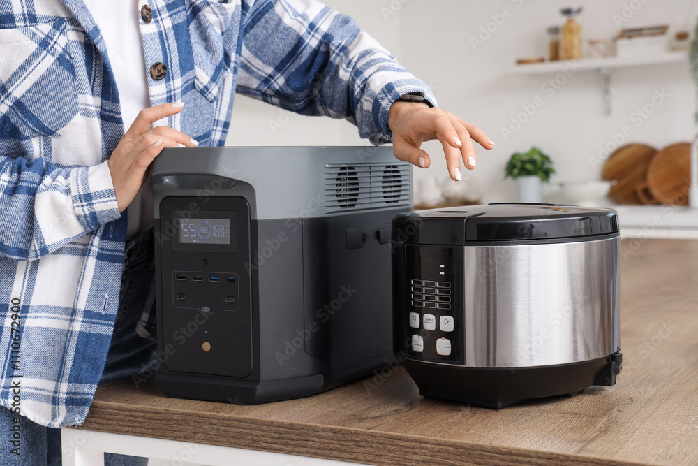 Woman with portable power station and multi cooker on table in kitchen