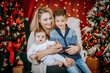 © Raivo - A mother sits with her two children, sharing a moment of joy and connection, surrounded by festive Christmas trees, lights, and decorations..