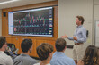 © PHAISITSAWAN - A stock market analyst is presenting a report to a group of investors using a screen to analyze data