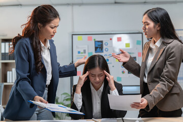 Wall Mural - Stressed businesswomen argue while their colleague suffers a headache in a tense office scene with paperwork and computers