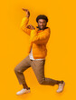 © Prostock-studio - Funny black guy fooling, dancing in egypt style, wearing glasses and winter jacket on orange studio background