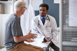 © Seventyfour - Waist up portrait of serious African American doctor wearing lab coat and holding tablet while listening to senior patient during discussion in clinic, copy space
