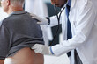 © Seventyfour - Side view close up of African American doctor using stethoscope while carefully examining back of senior patient during checkup in clinic, copy space