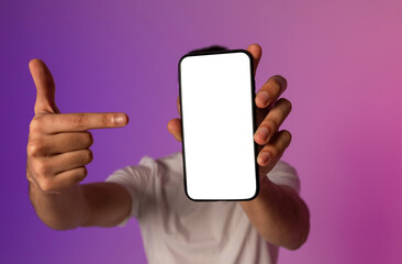 Poster - Unrecognizable young man holding smartphone in front of his face, pointing at empty screen, offering space for mobile app or website, demonstrating mockup for online ad in neon light, selective focus