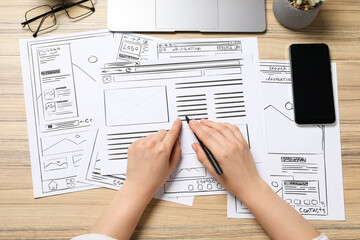 Leinwandbilder - Website designer creating wireframe on paper with pen at wooden table, top view