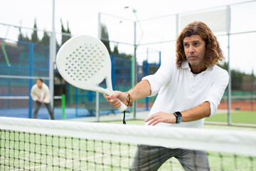 Wall Mural - Portrait of middle-aged Latin male in sportswear enjoying popular sport padel game on tennis court outside