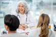 © Kittipong - A professional senior Asian female doctor in a uniform having a consultation with a young married couple in the examination room. doctor visit, health care, medical
