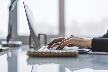 Poster - In a blurry office environment, a close-up view reveals a woman's hands typing on a trendy laptop keyboard