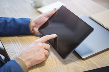 Wall Mural - Detailed image of a male hand interacting with a digital tablet on a desk, amidst the vague surroundings of a bright office setting