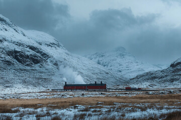 Canvas Print - Snow-covered mountains surround a steam-emitting building in winter