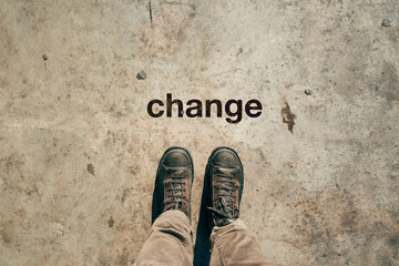 Feet in boots from above with word Change printed on sidewalk