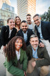 © Jose Calsina - Vertical. Diverse group of business professionals smiling and looking at the camera during an outdoor meeting, showcasing teamwork. Successful businesspeople looking at camera together at the downtown