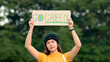 © ChayTee - Go green Gen Z woman asia young people looking at camera stress showing save the earth planet world care banner poster sign in city nature tree. Protect global warming future asian hope net zero waste