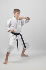 Fifteen year old male teenage karate black belt standing in a low stance doing a back fist, studio shot against a white background