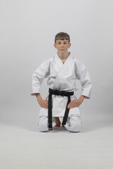 Fifteen year old male teenage karate black belt kneeling, studio shot against a white background