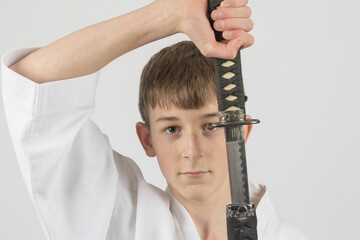 Fifteen year old male teenage karate black belt drawing a katana, studio shot against a white background